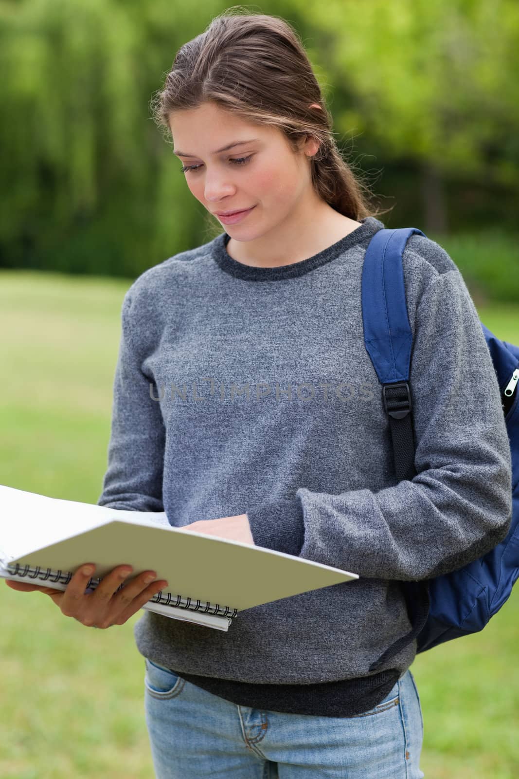 Young woman reading her notebook while standing up in a park by Wavebreakmedia