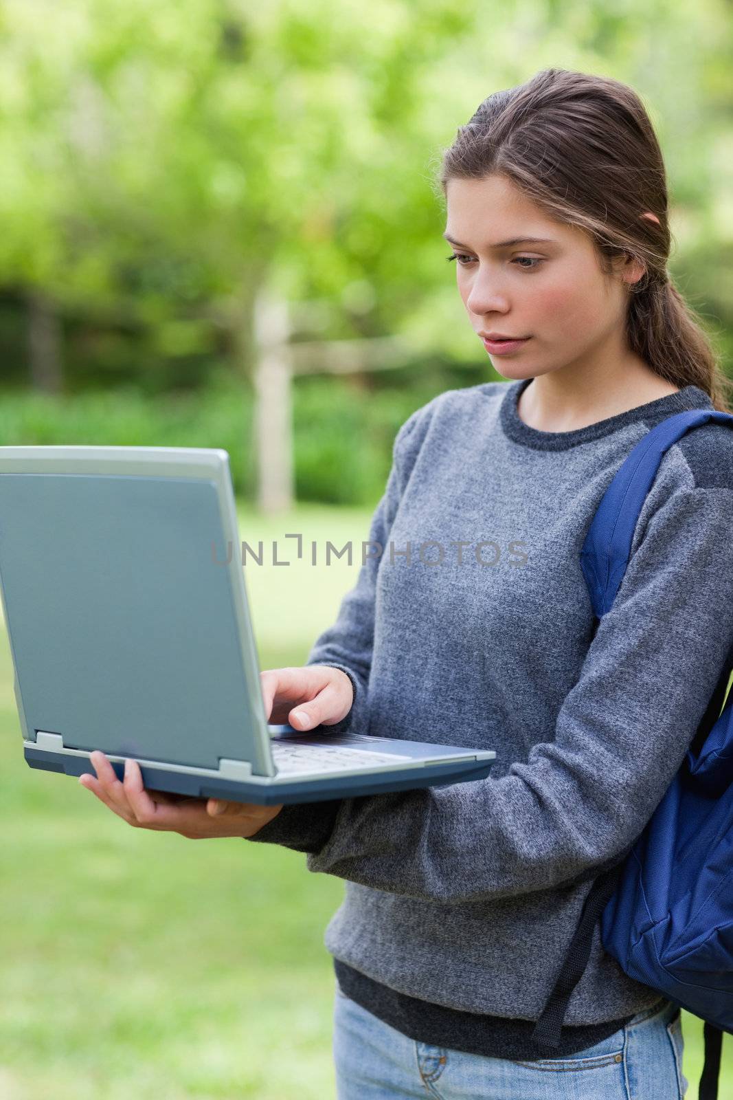 Serious student typing on her laptop while standing upright in a by Wavebreakmedia