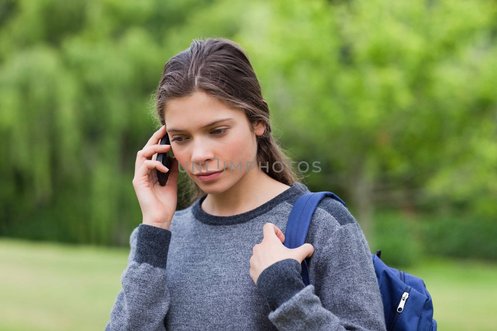 Young calm girl using her cellphone while carrying her backpack