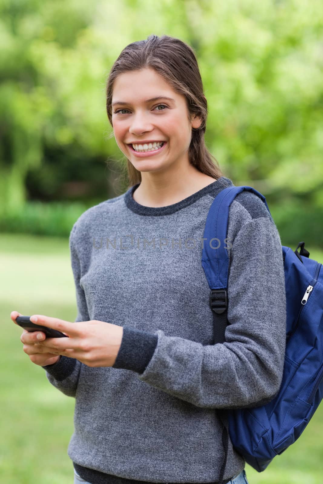 Happy teenager standing in the countryside while sending a text with her cellphone