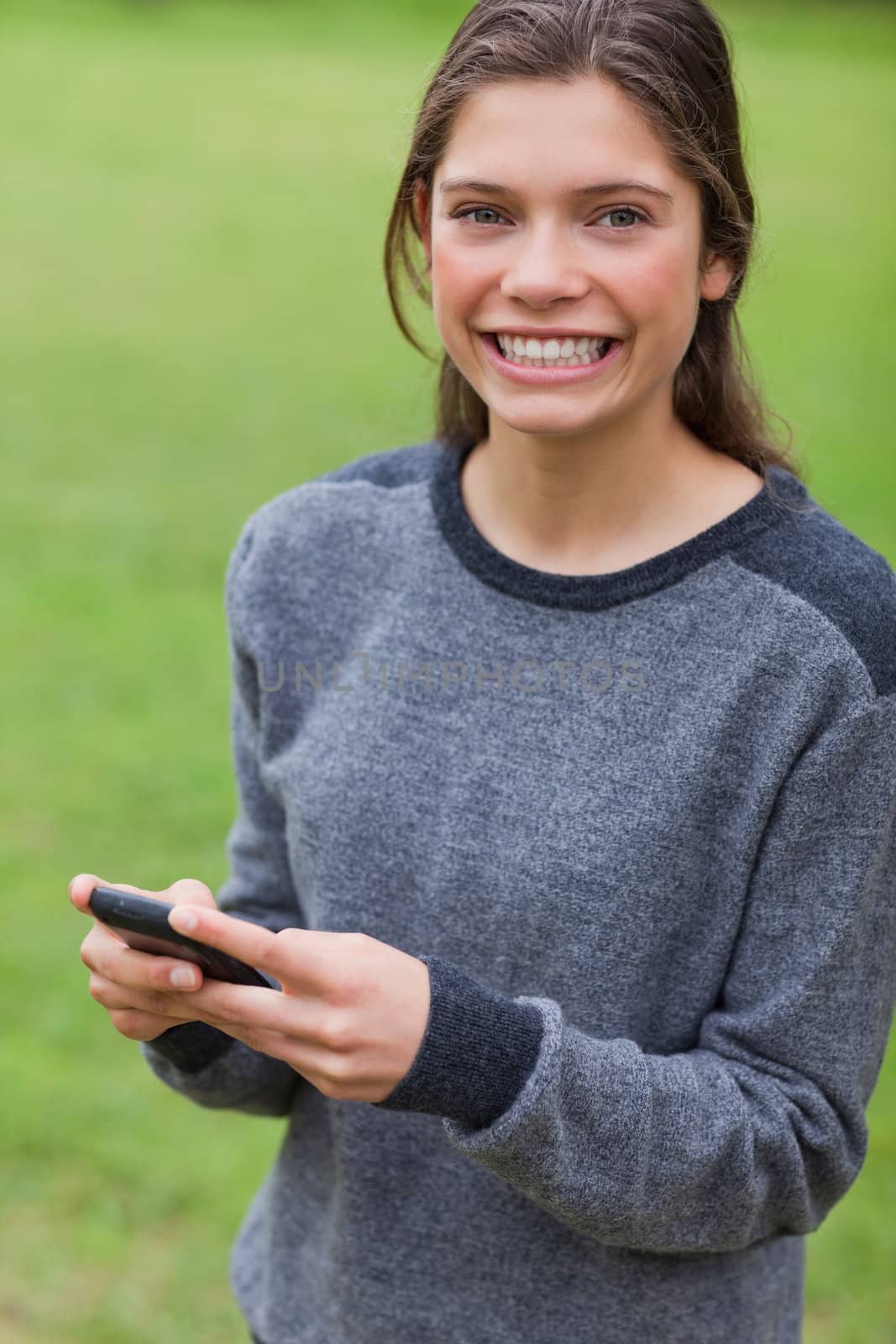Young smiling adult looking straight at the camera while using her mobile phone