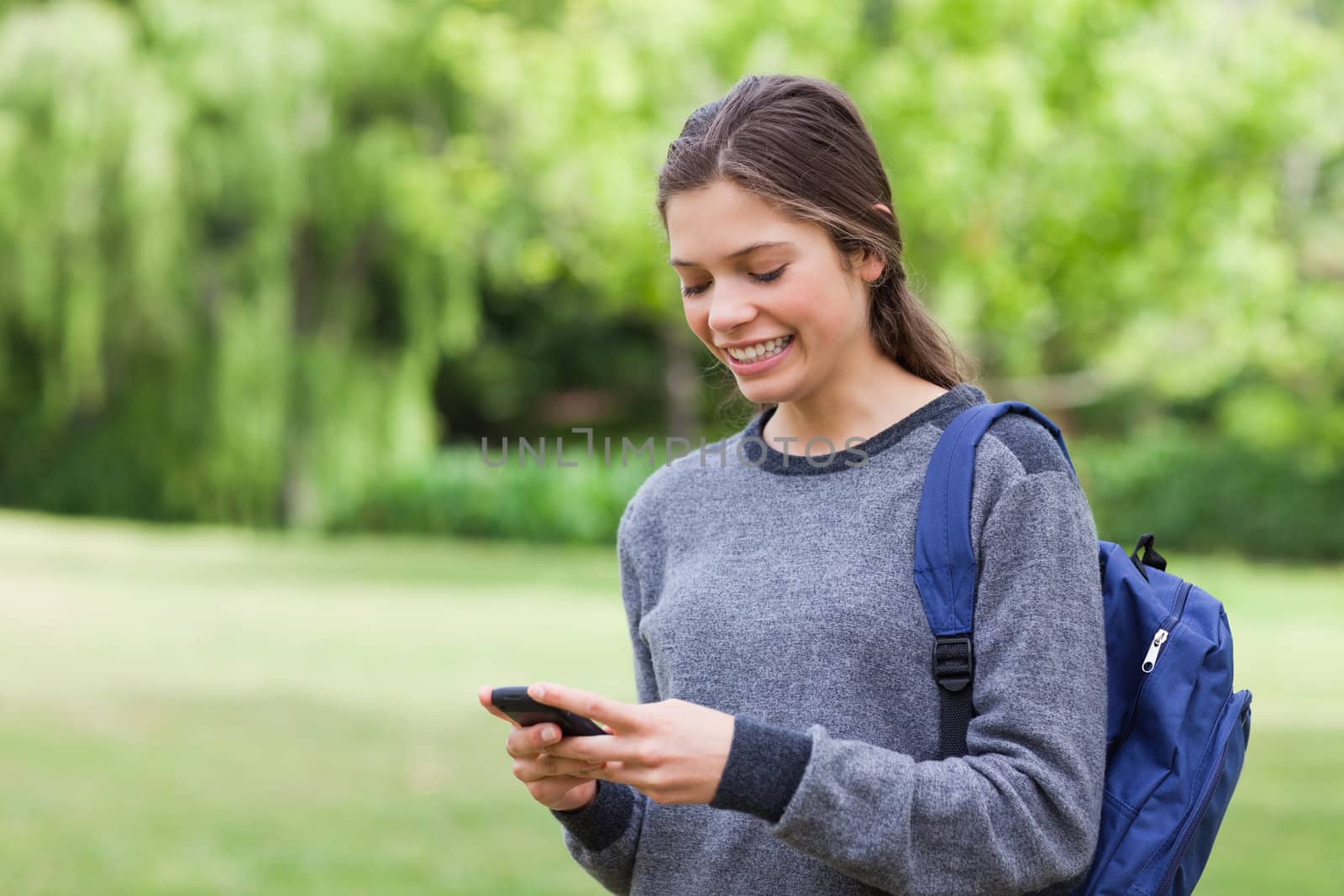 Smiling teenage girl using her cellphone while receiving a text by Wavebreakmedia