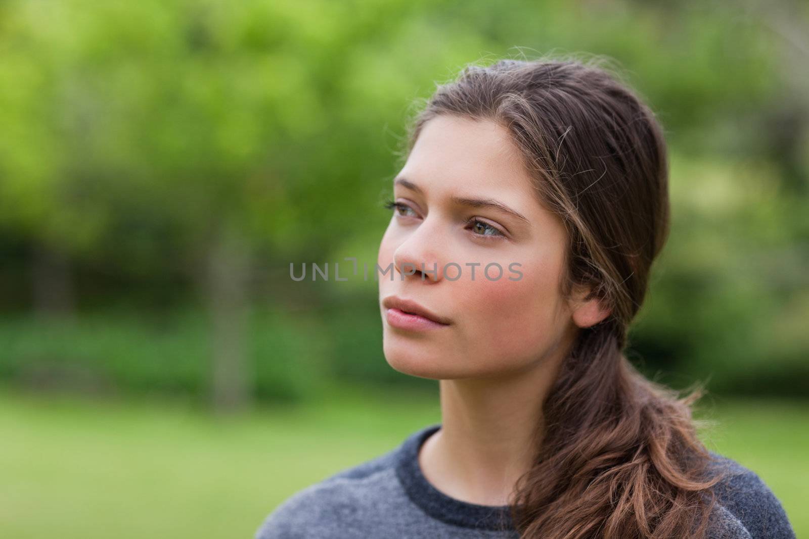 Thoughtful young woman standing in a park while looking towards  by Wavebreakmedia