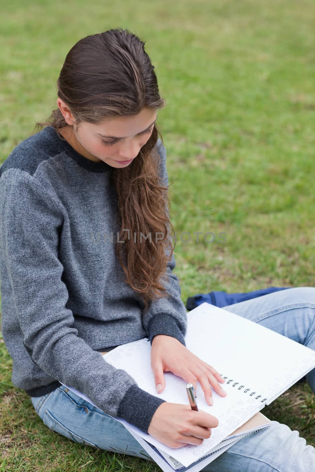 Serious student doing her homework while sitting on the grass in the countryside