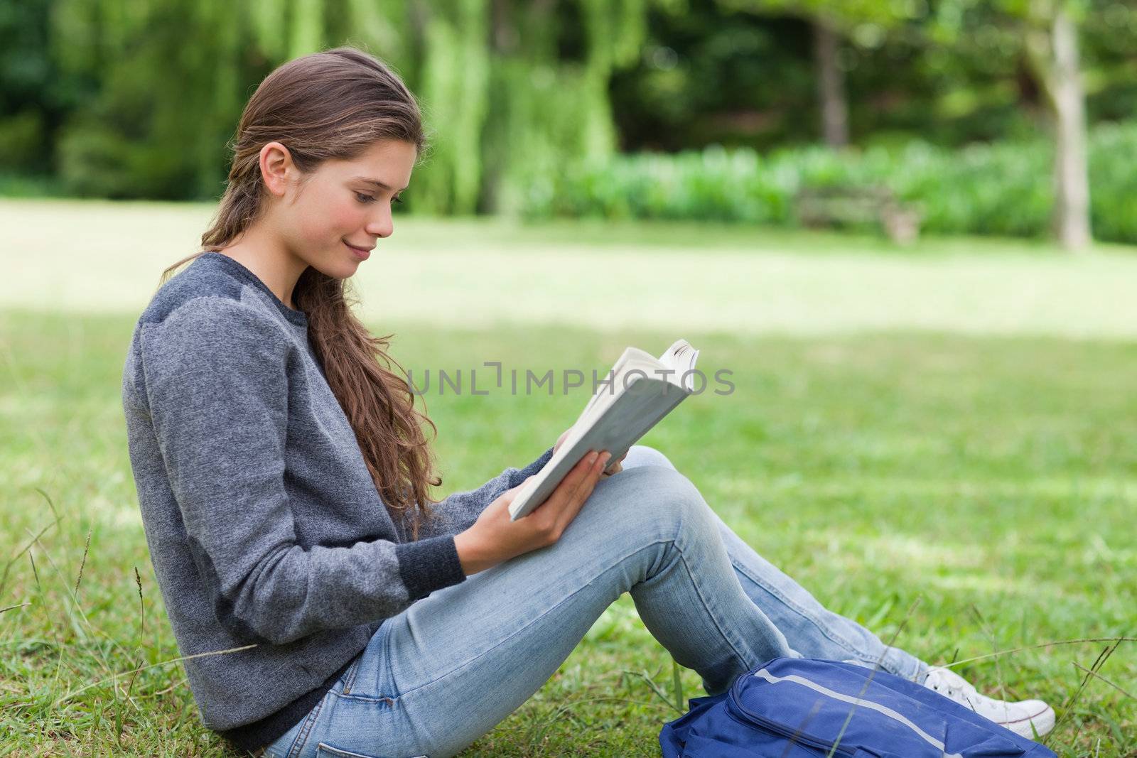 Young relaxed girl seriously reading a book while sitting on the grass in a park