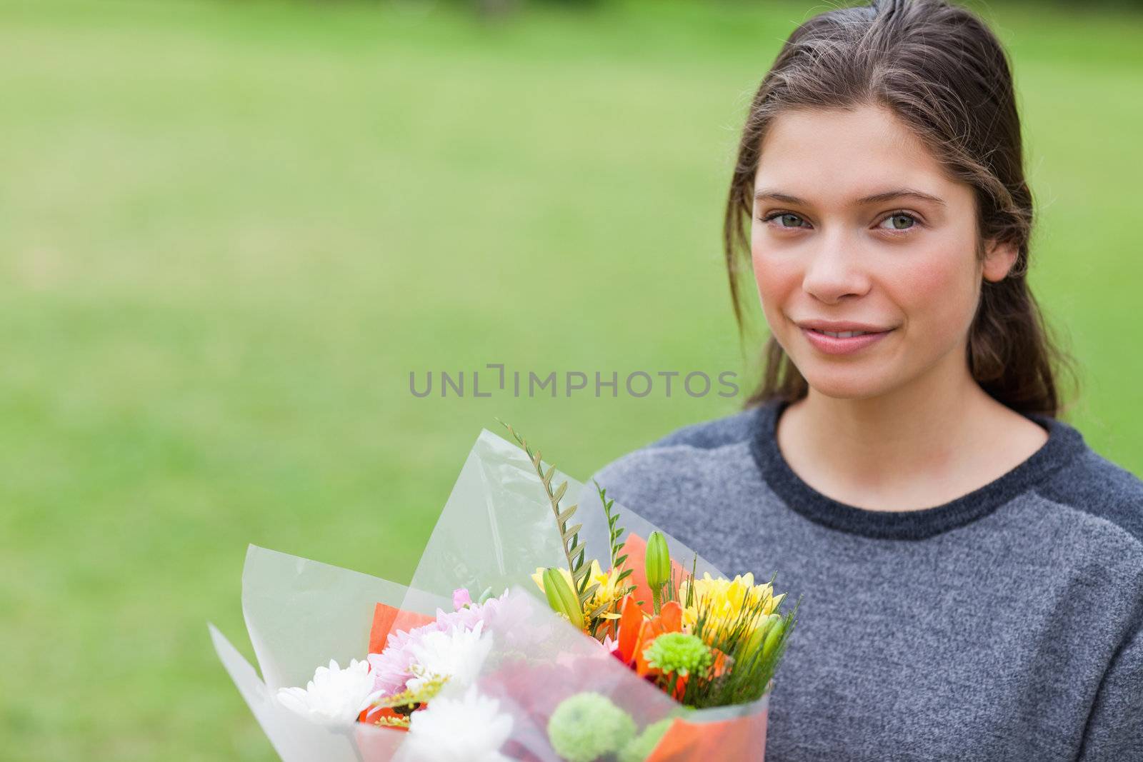 Calm teenager holding a beautiful bunch of flowers while standing up in a park
