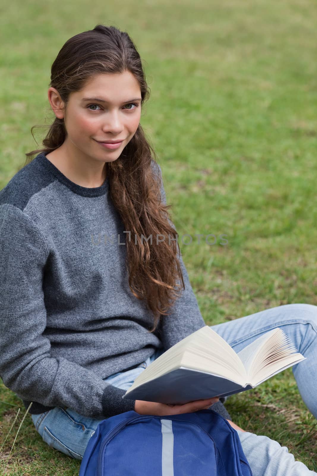 Calm student holding a book while sitting next to her backpack by Wavebreakmedia