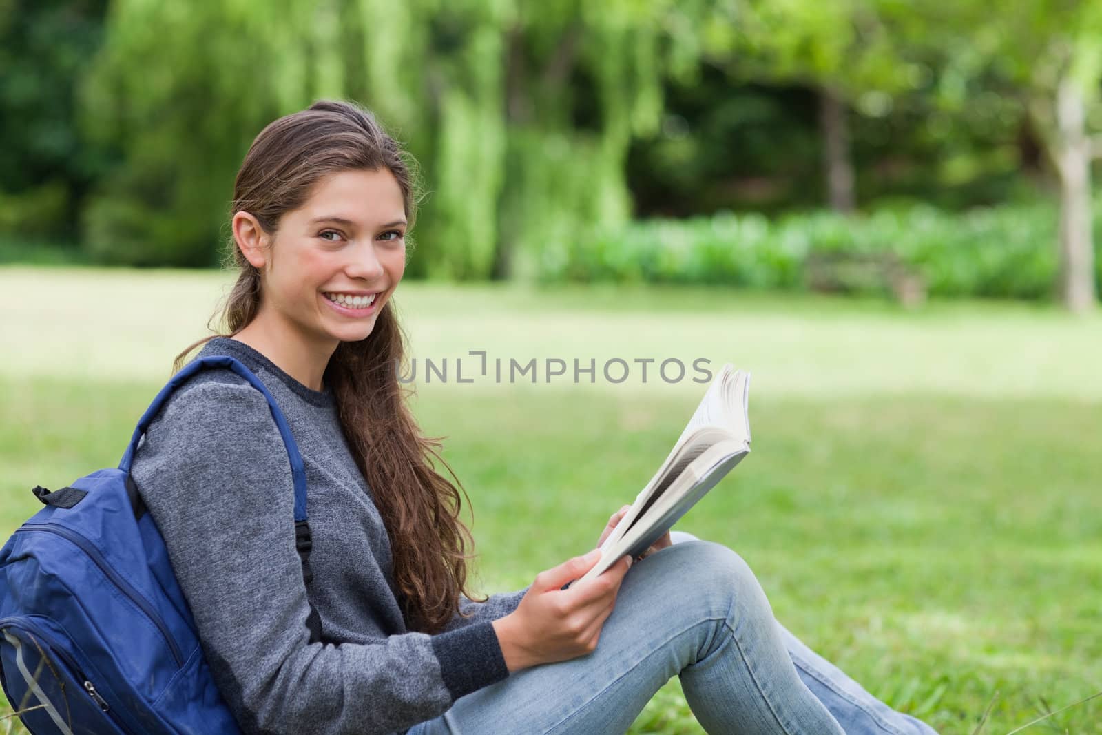 Young smiling girl reading a book while sitting on the grass by Wavebreakmedia