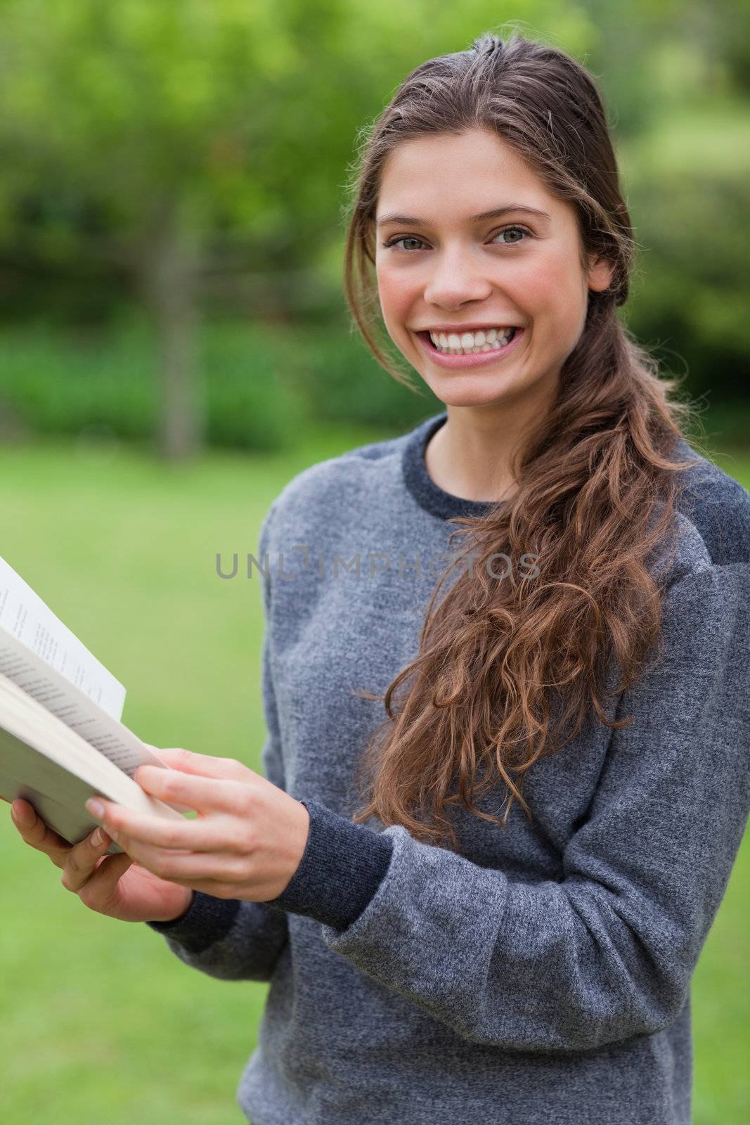 Young happy adult looking at the camera while reading a book in the countryside