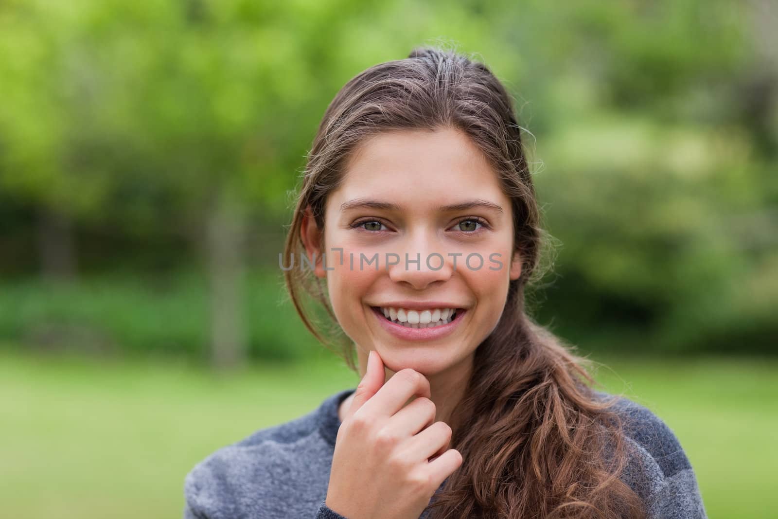 Smiling young adult placing her hand on her chin while standing up in the countryside