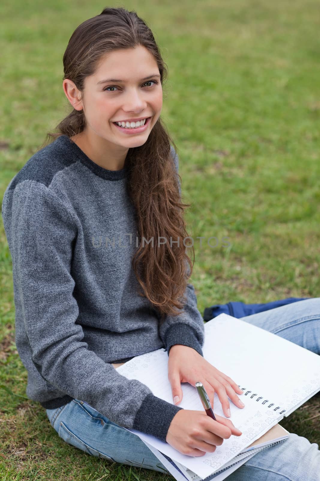 Smiling young woman writing on her notebook while sitting on the grass