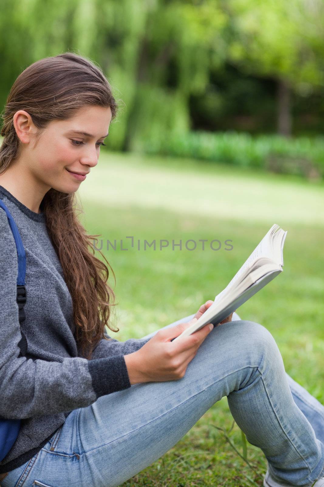 Young smiling woman reading a book while sitting on the grass in by Wavebreakmedia
