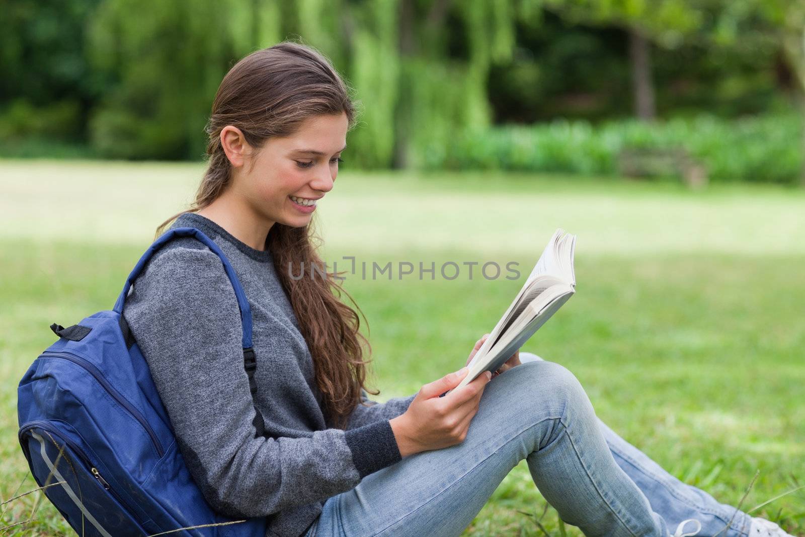 Young calm girl sitting on the grass while attentively reading a book
