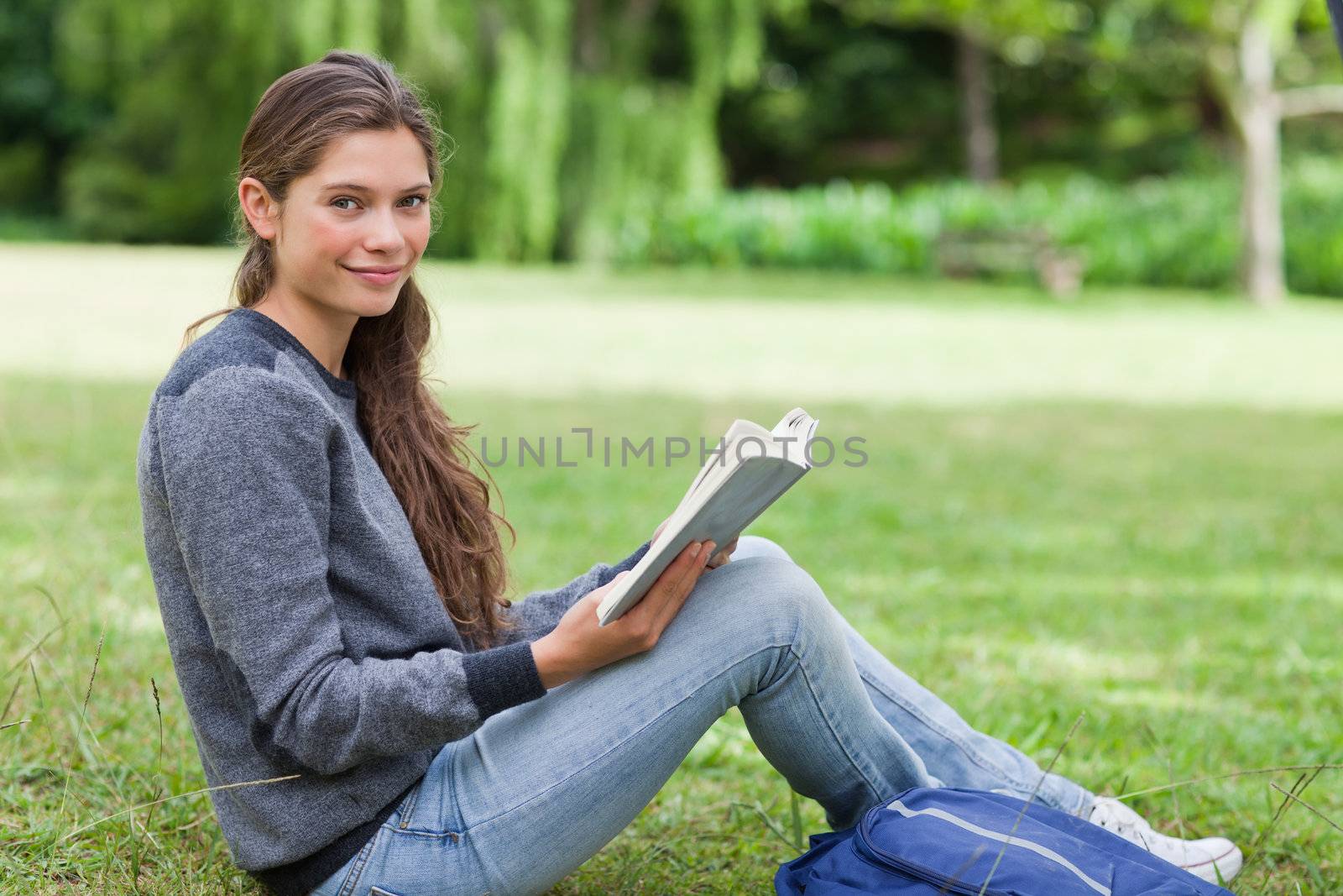 Smiling girl holding a book on her knees while sitting on the grass in the countryside