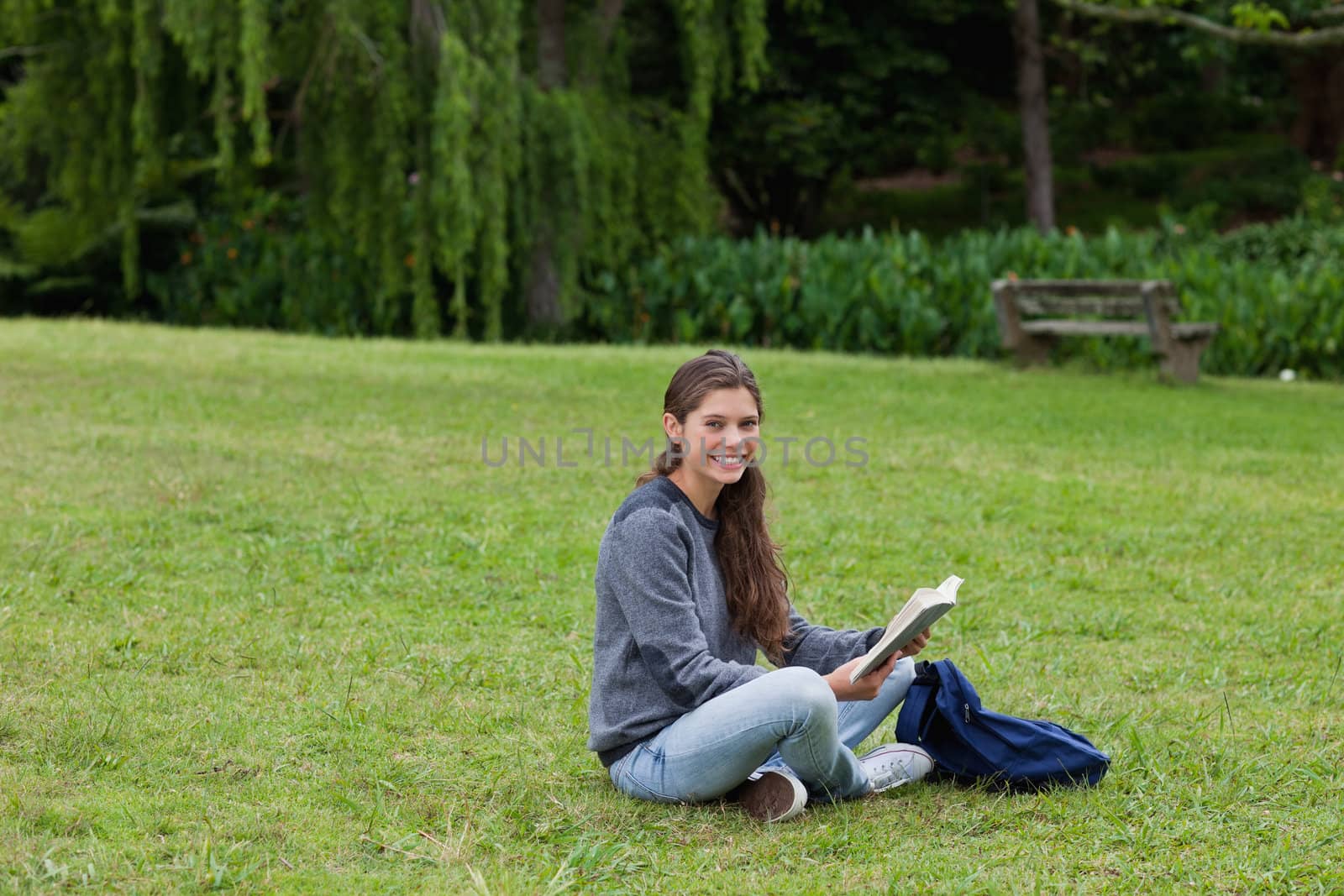 Smiling young adult reading a book while sitting cross-legged on the grass in a park