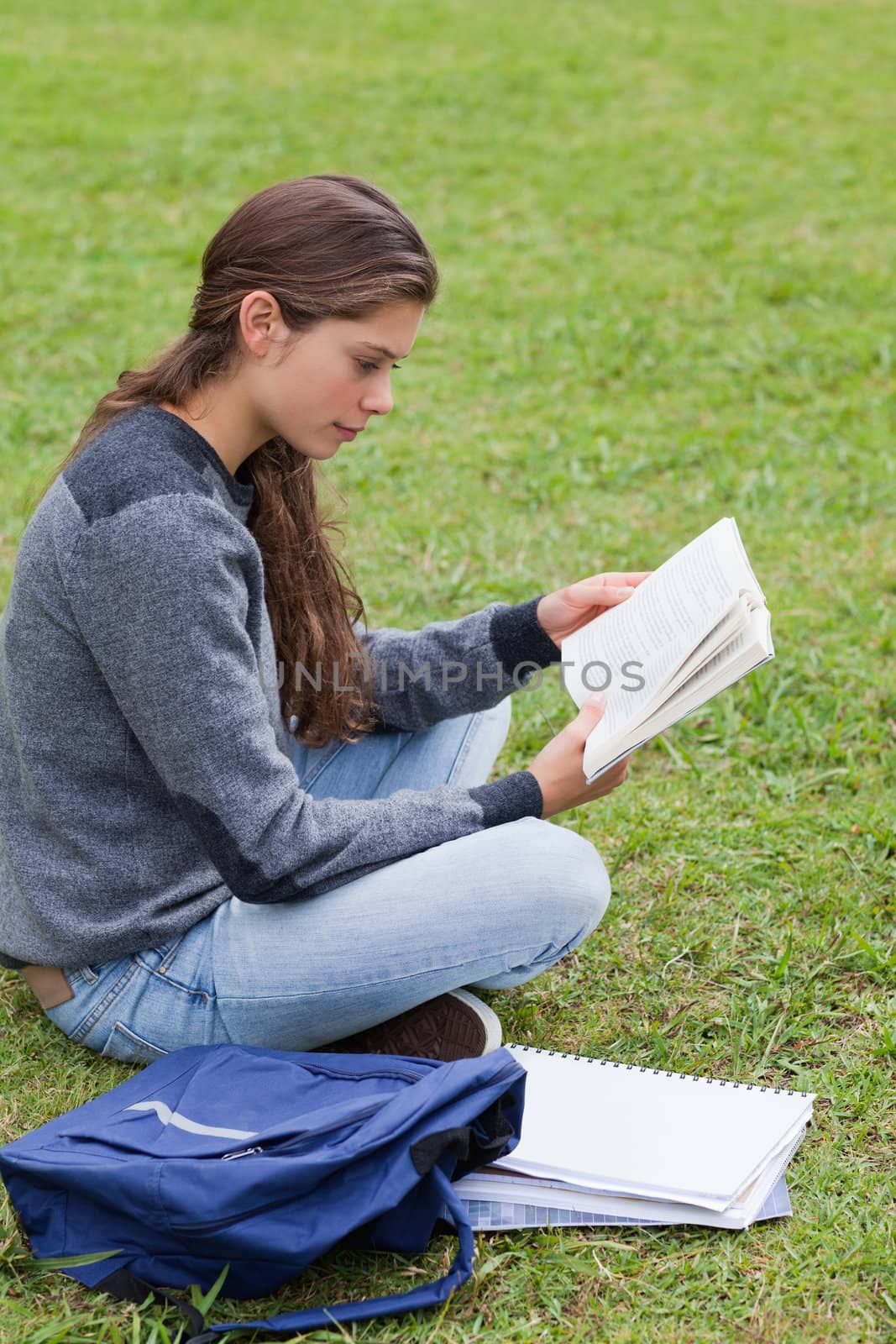Young serious girl reading a book while sitting cross-legged by Wavebreakmedia