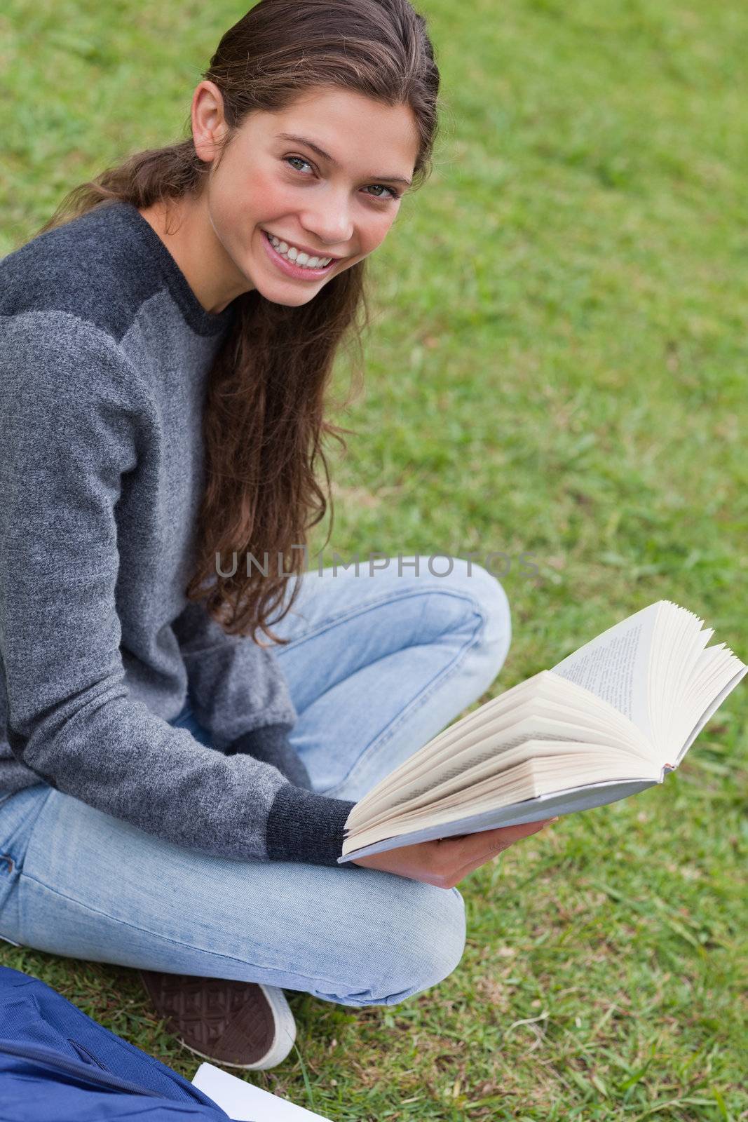 Young smiling woman sitting cross-legged in a park while holding by Wavebreakmedia