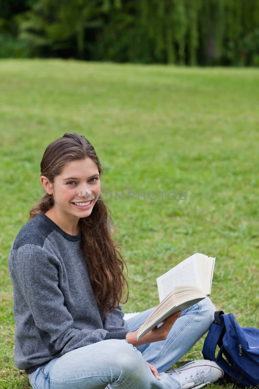Young smiling girl sitting cross-legged while holding a book by Wavebreakmedia