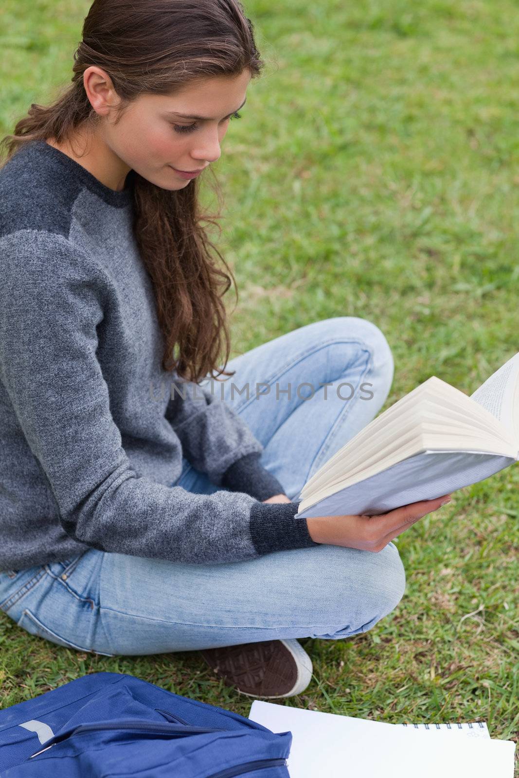 Relaxed young girl reading a book while sitting down on the grass in the countryside