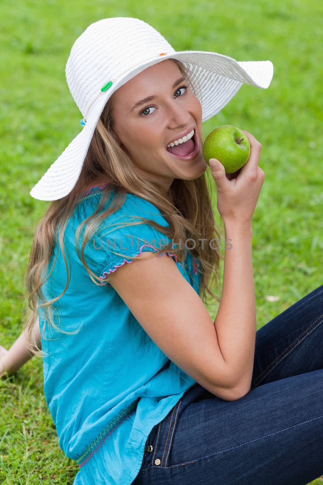 Happy young girl eating a green apple while sitting on the grass by Wavebreakmedia
