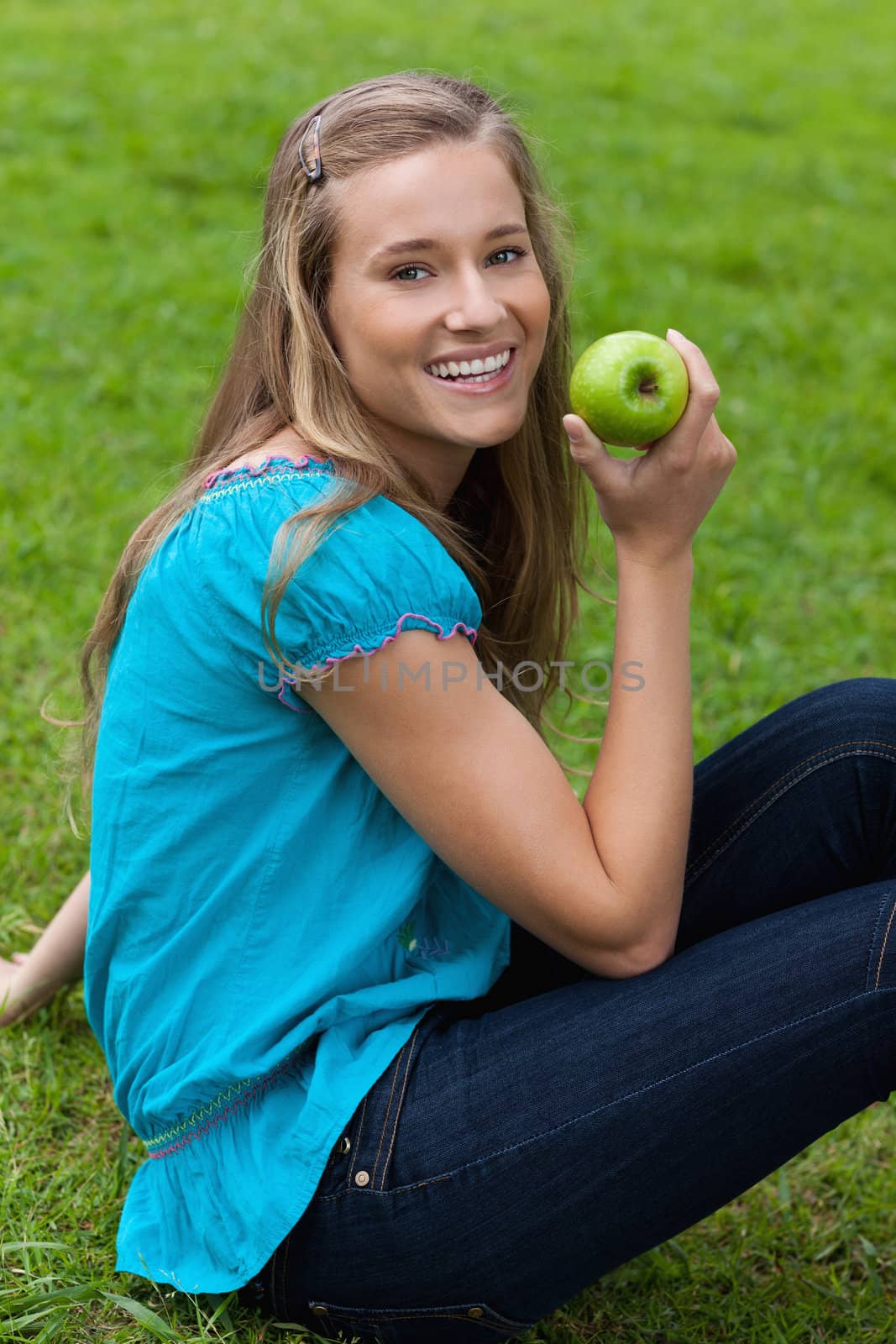 Smiling young woman holding a green apple while sitting in a par by Wavebreakmedia