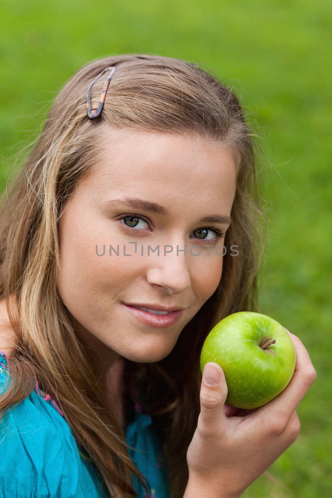 Attractive young girl holding a green apple while standing upright in the countryside