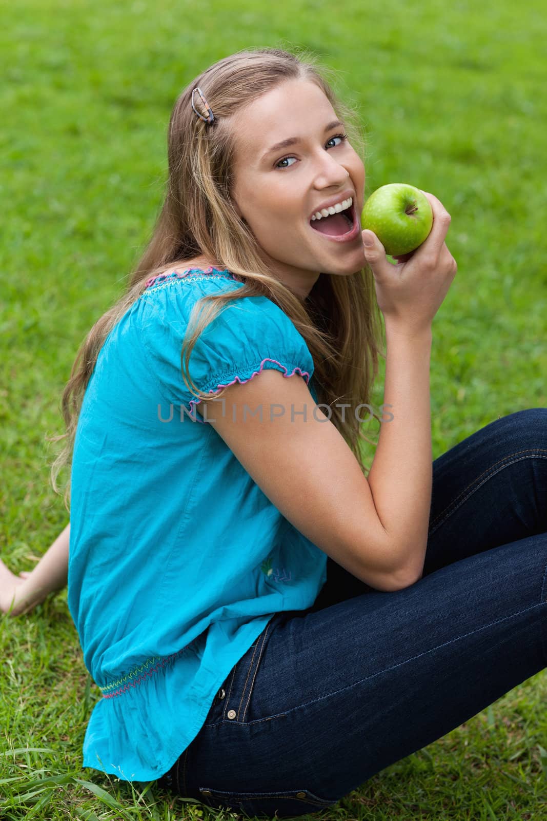 Young smiling woman eating a green apple while sitting in a park by Wavebreakmedia