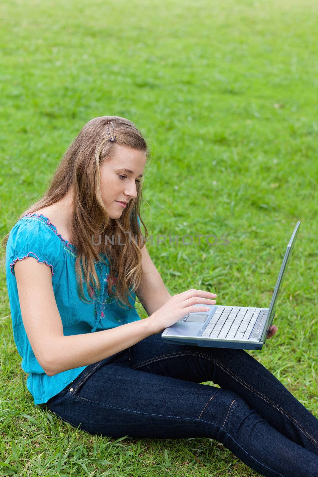 Young relaxed girl using her laptop while sitting down in the countryside