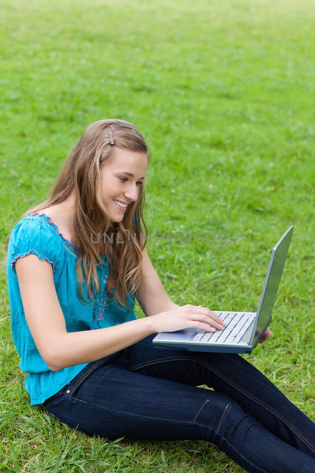Young smiling girl typing on her laptop while sitting on the grass in the countryside