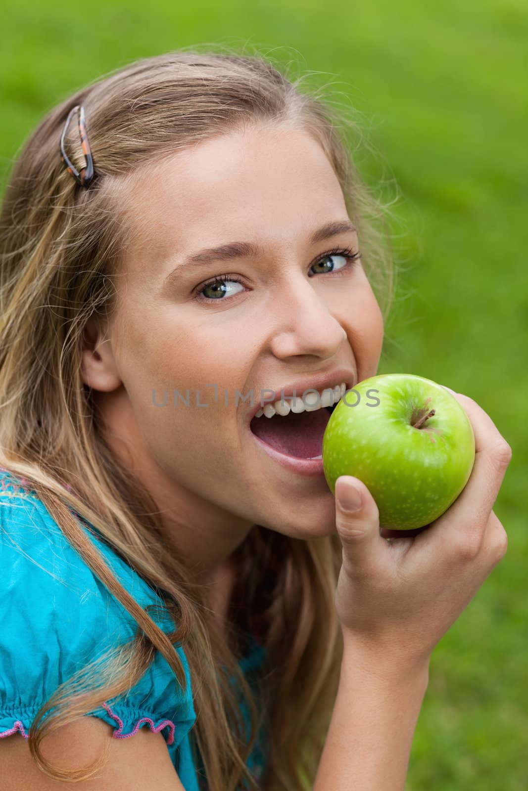 Young happy woman looking at the camera while eating a delicious green apple