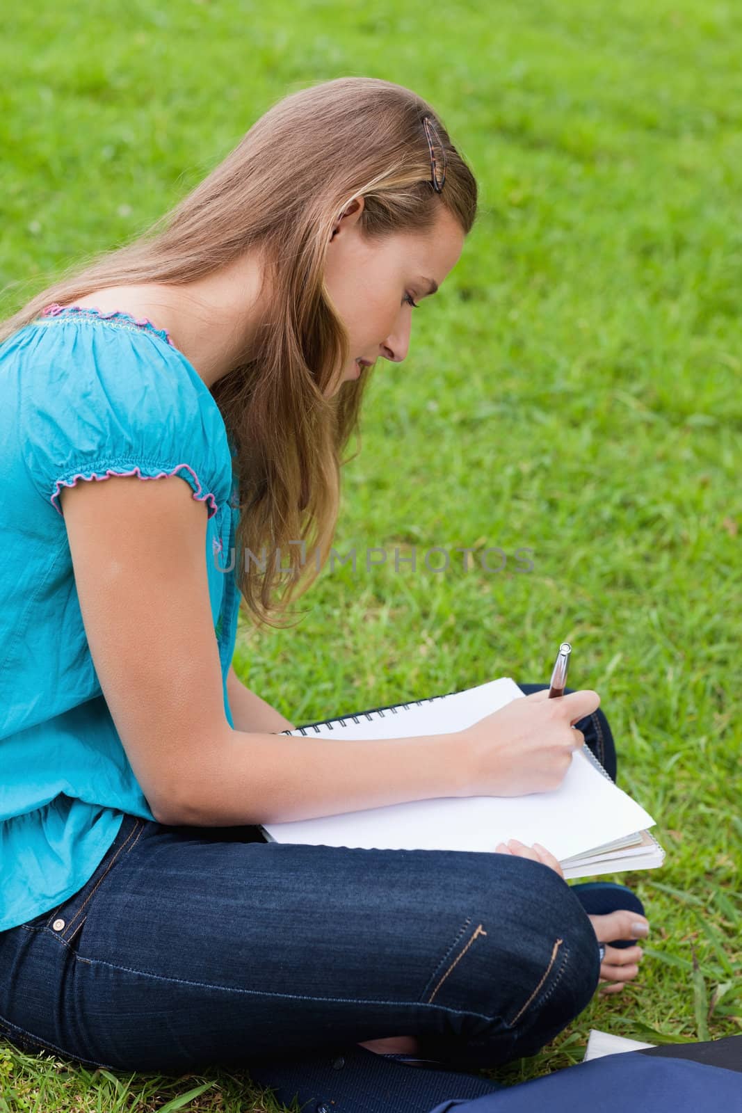 Young girl writing on her notebook while sitting down on the grass in the countryside