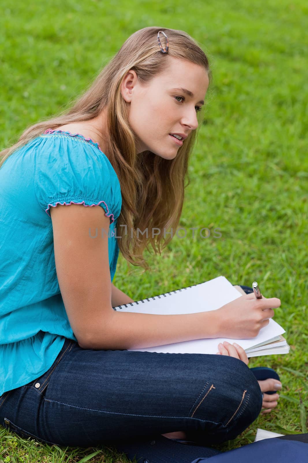 Attractive young girl sitting down in a park while doing her hom by Wavebreakmedia