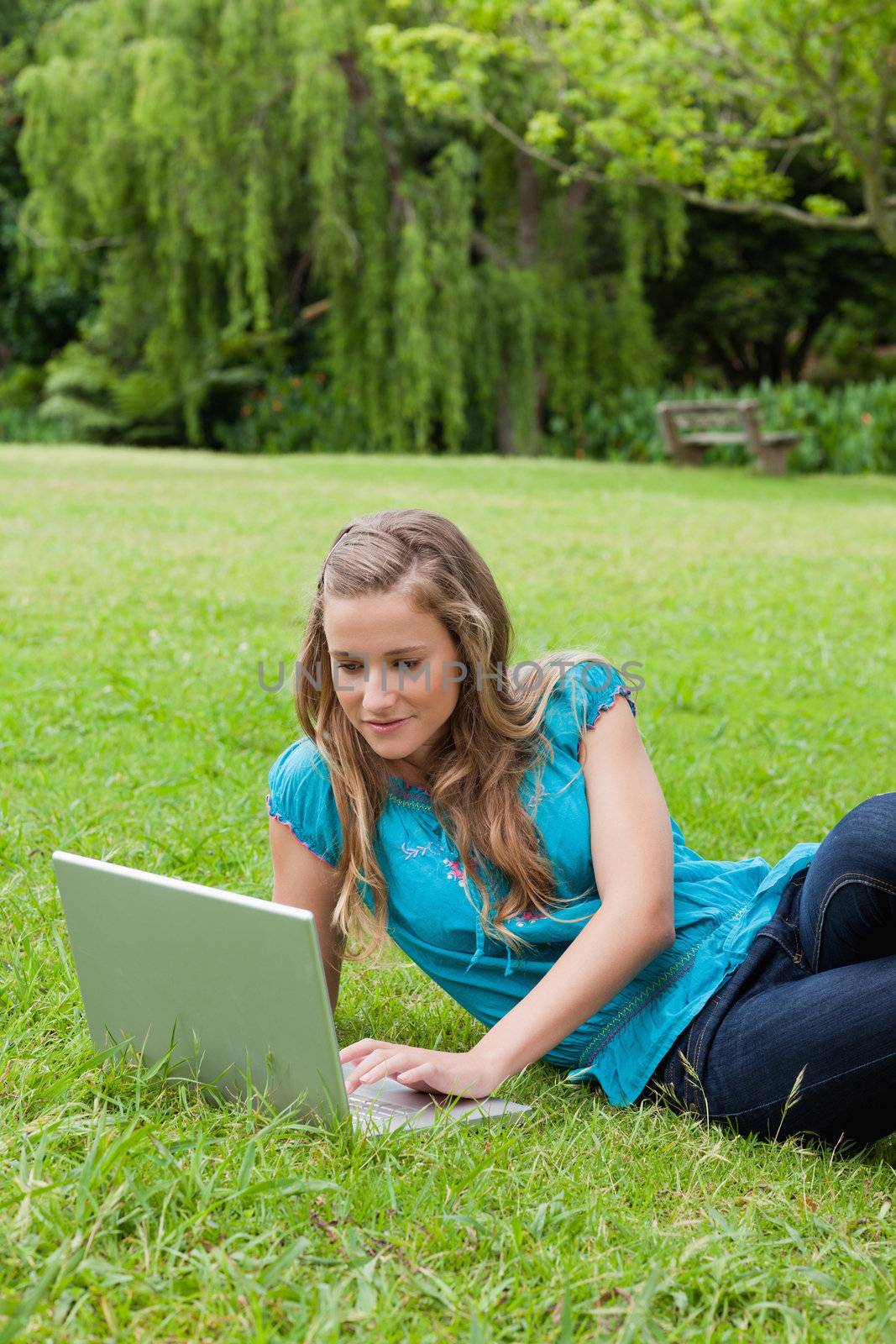 Young calm girl lying on the side on the grass while working on her laptop in a park