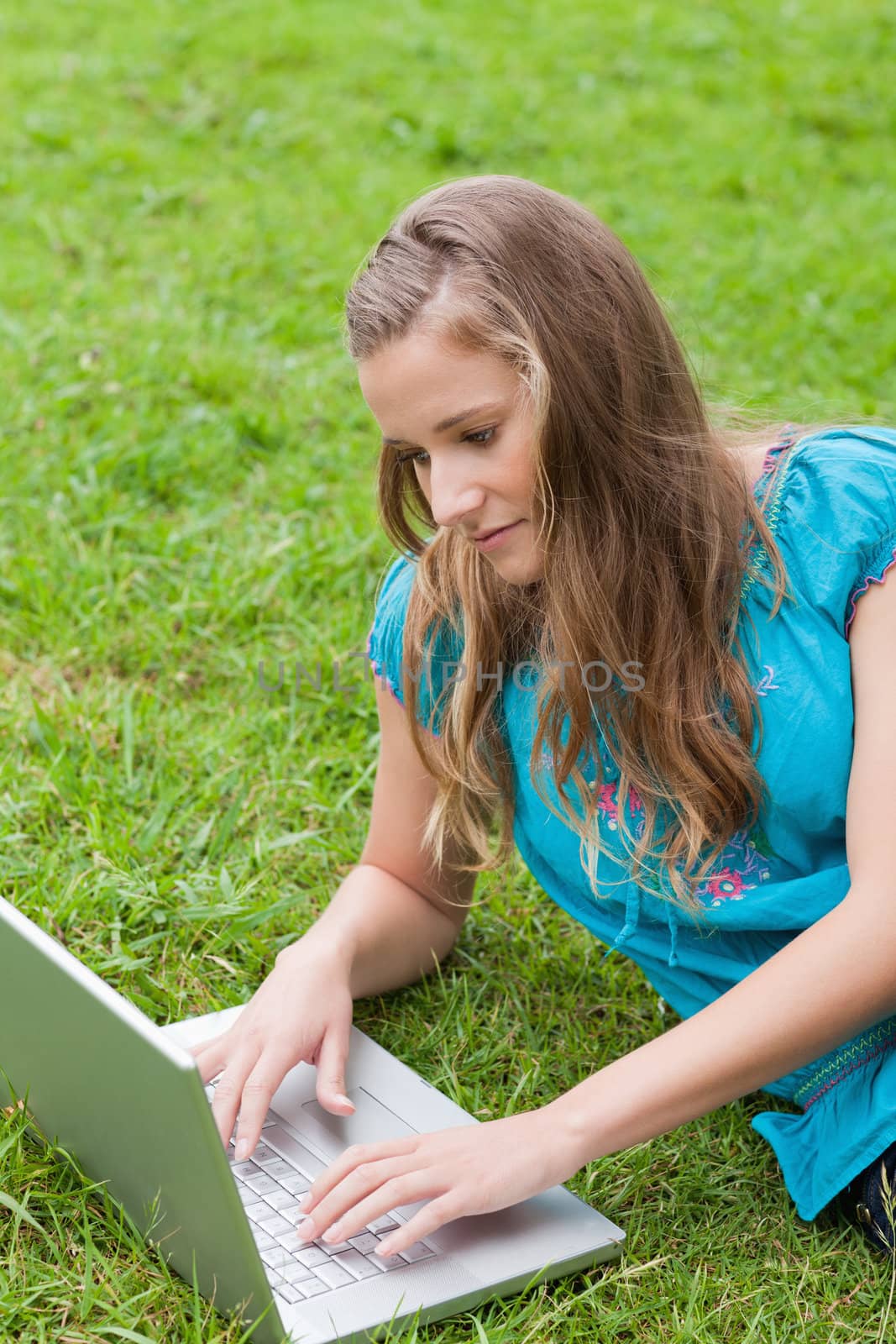 Young serious student lying on the grass in the countryside while using her laptop