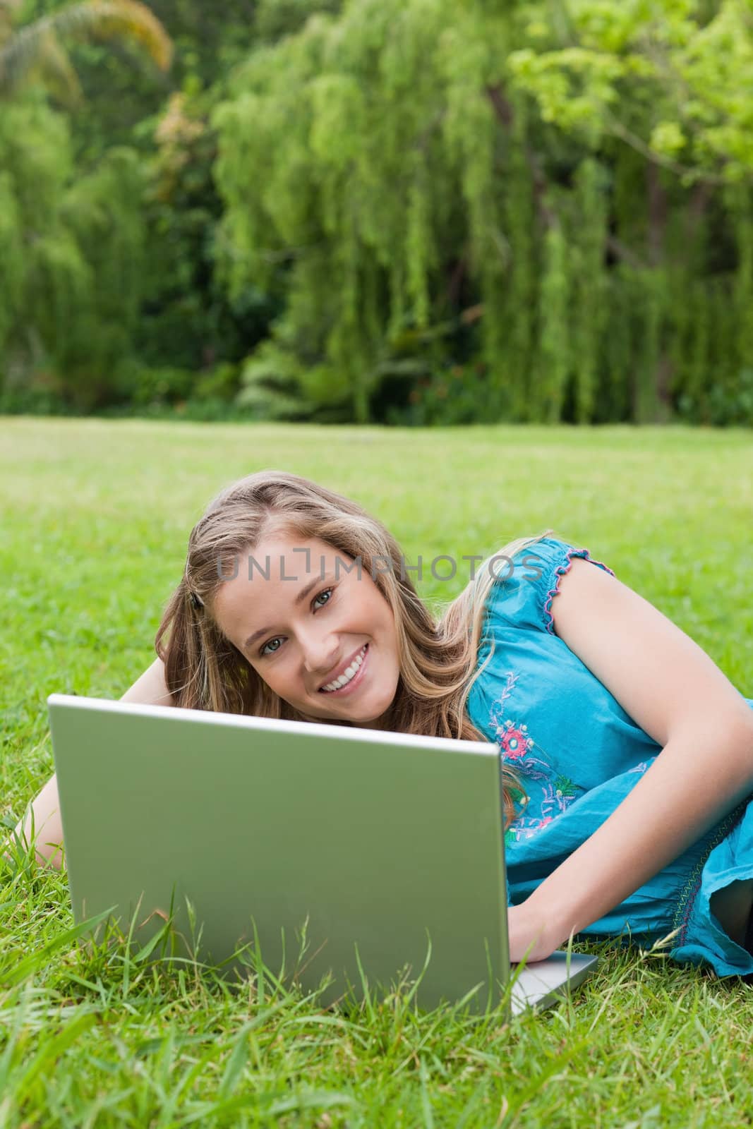 Young smiling girl using her laptop while lying on the grass by Wavebreakmedia