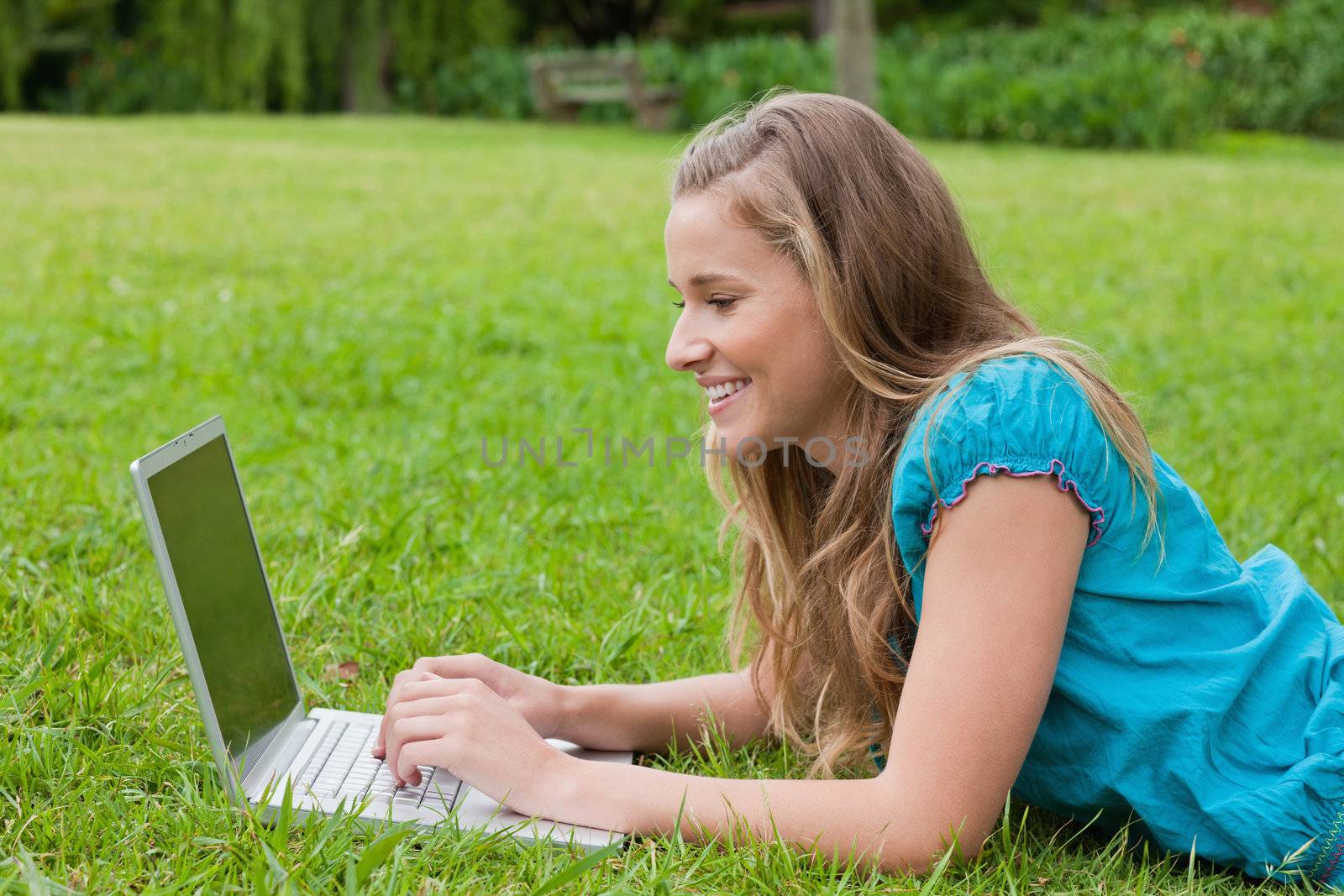 Young smiling girl looking at her laptop while lying on the grass in the countryside