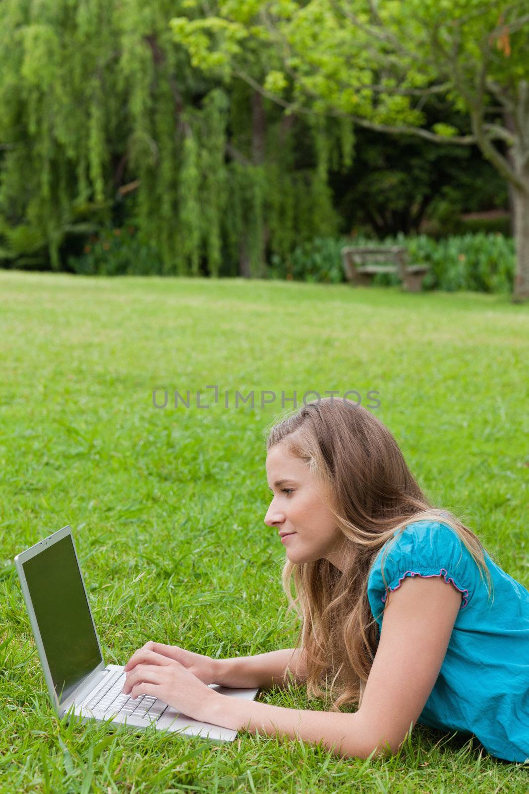 Side view of a young student using her laptop while lying on the grass in a park