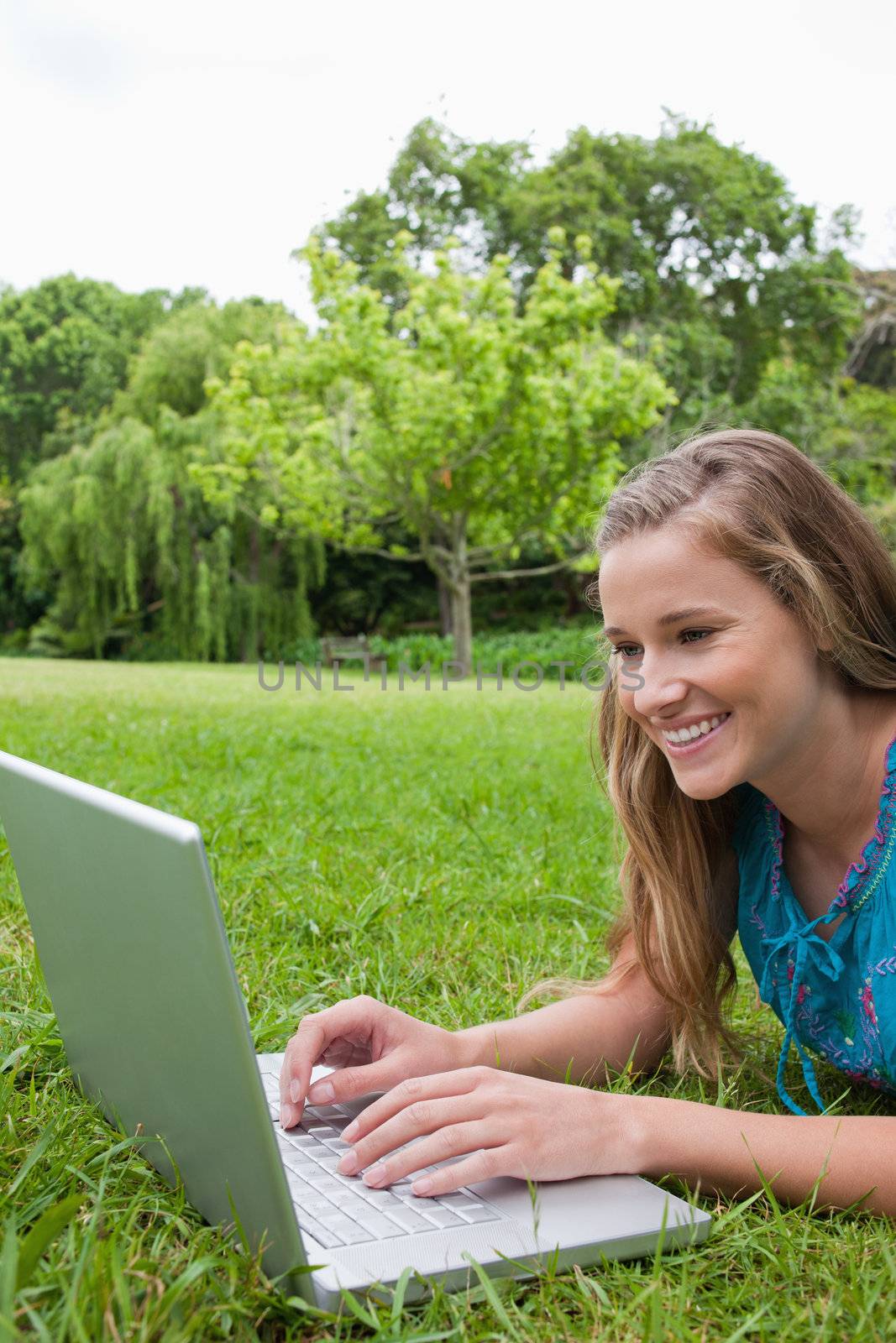 Young happy student using her laptop in the countryside while lying on the grass