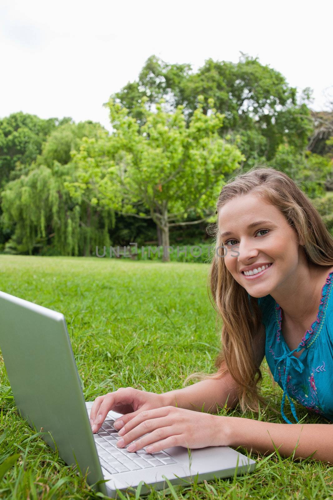 Smiling teenager looking at the camera while using her laptop by Wavebreakmedia