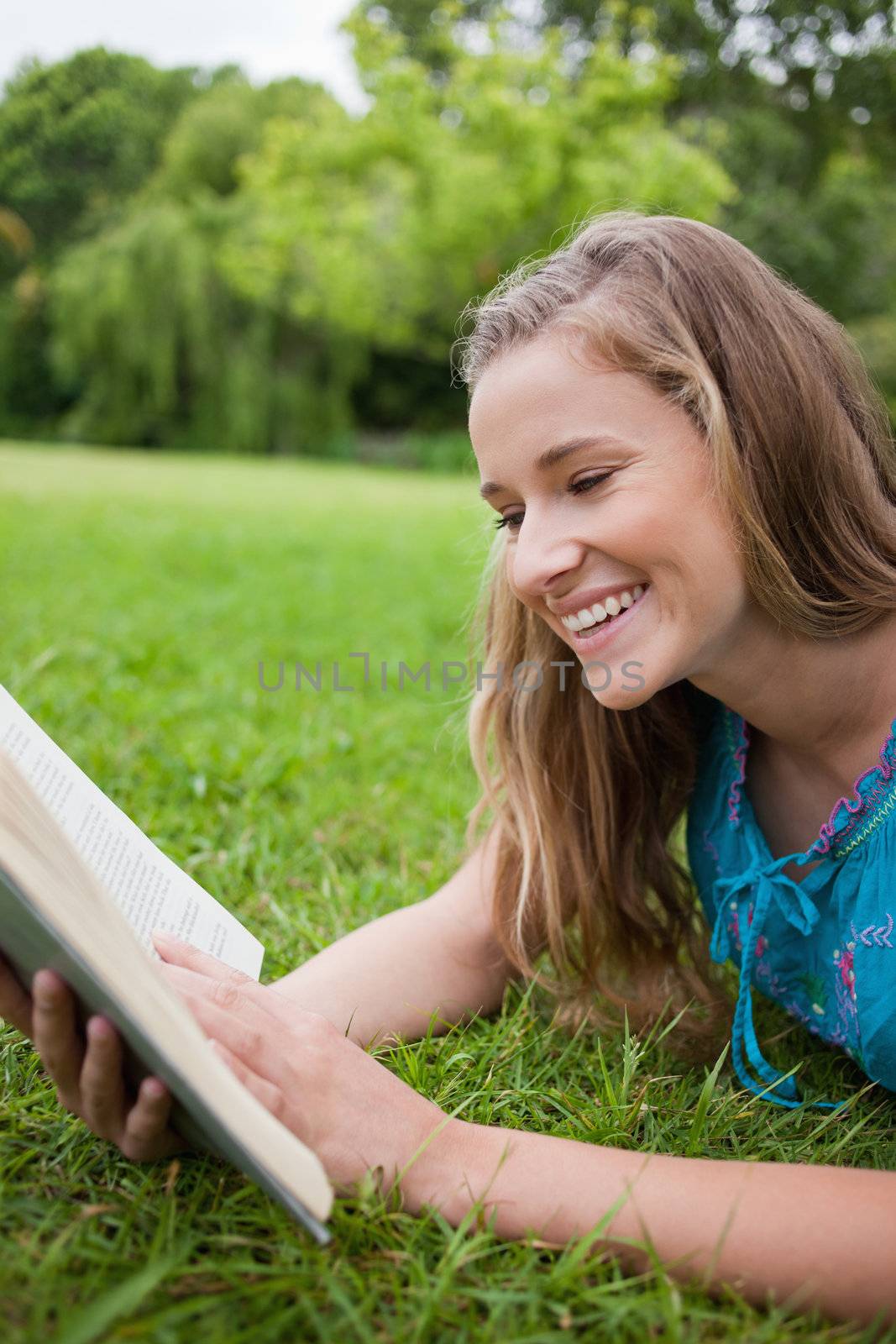 Young girl reading a book in a parkland while laughing by Wavebreakmedia