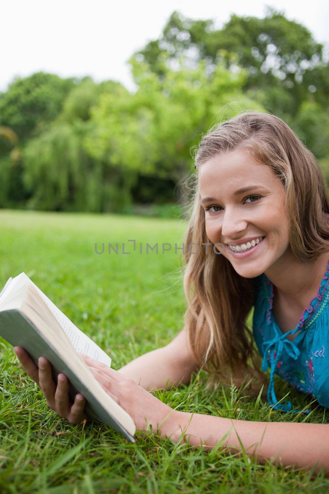 Happy student lying on the grass in the countryside while holding a book