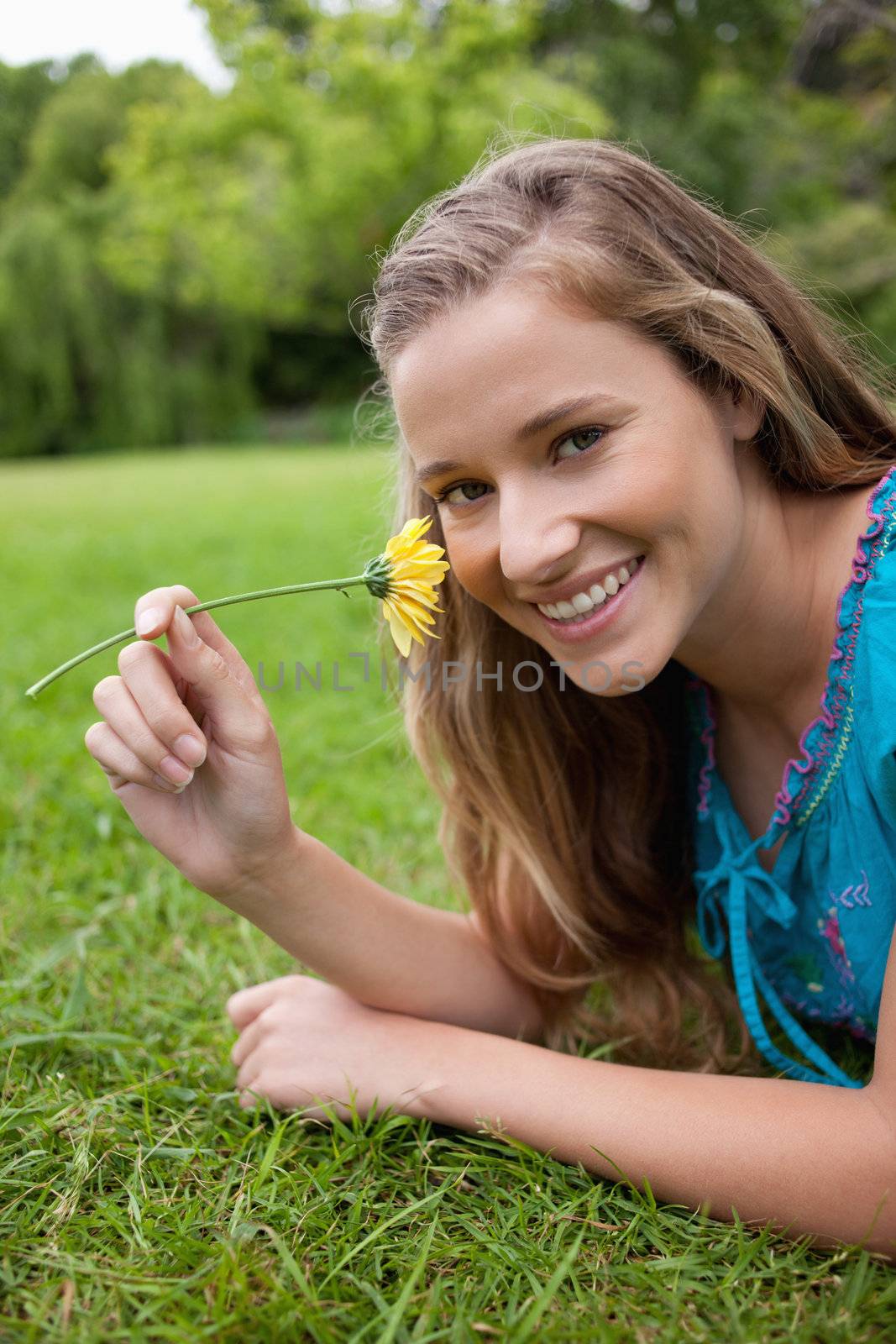 Young smiling girl smelling a yellow flower while lying on the g by Wavebreakmedia