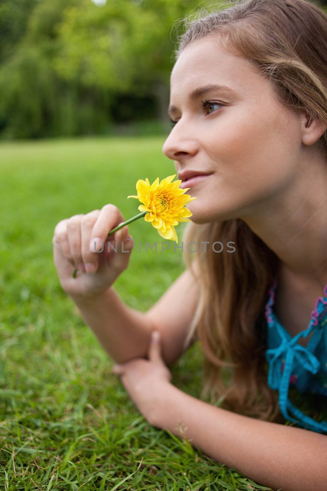 Young girl lying on the grass while smelling a flower by Wavebreakmedia