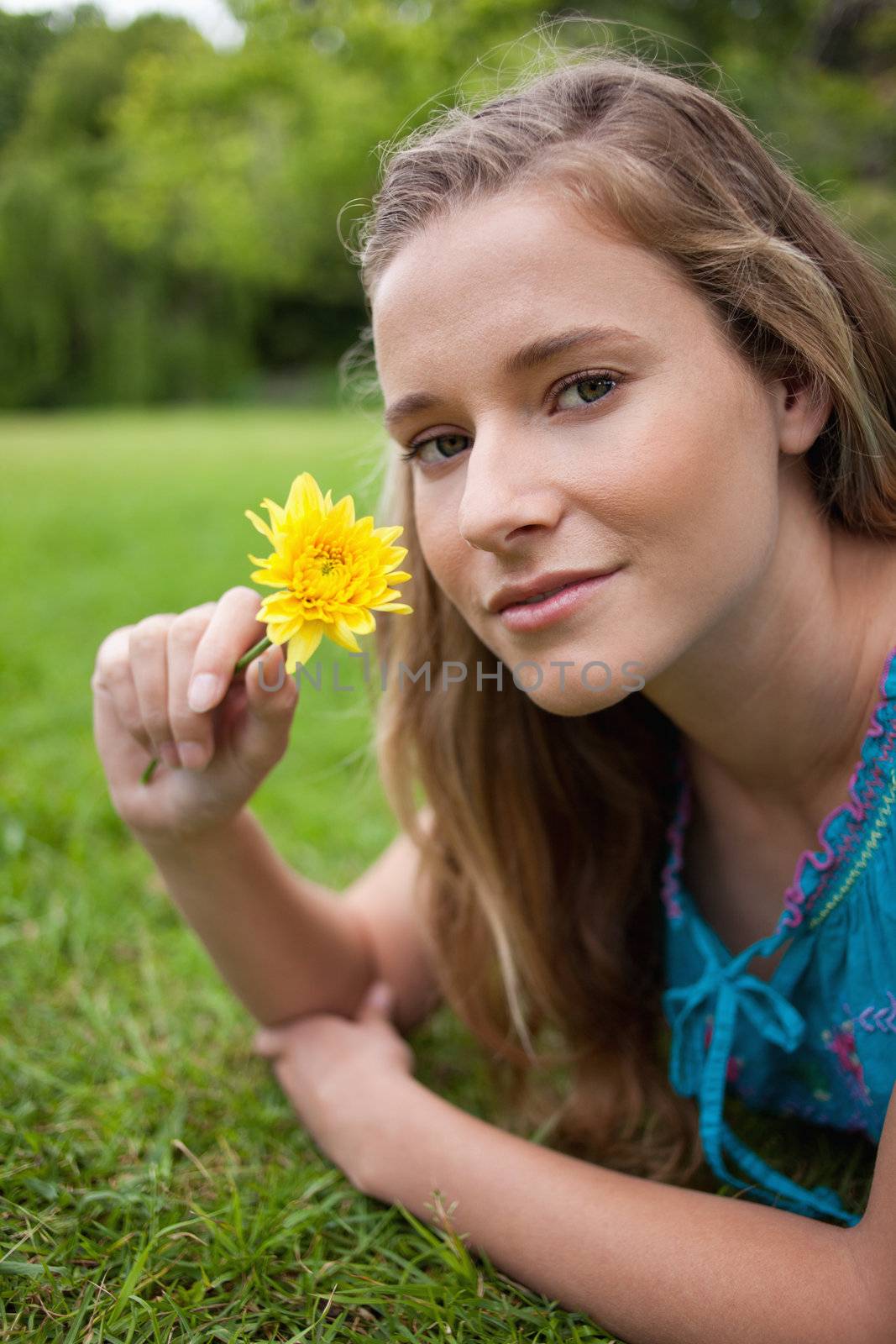 Young relaxed girl lying on the grass in the countryside while holding a yellow flower