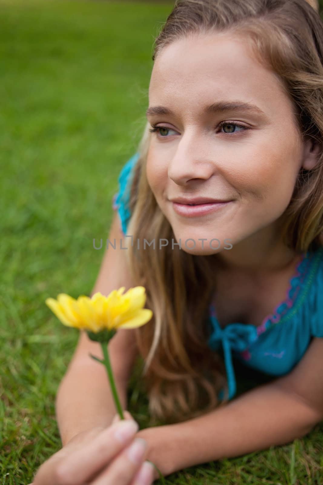 Young thoughtful girl lying on the grass in the countryside while holding a yellow flower