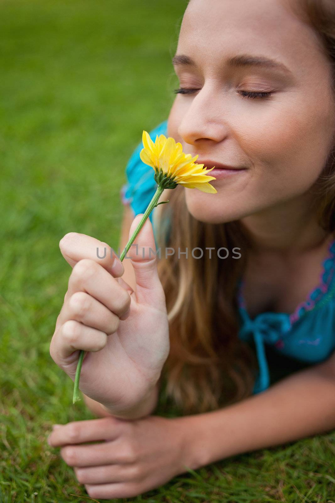 Young relaxed girl smelling a flower while lying on the grass by Wavebreakmedia