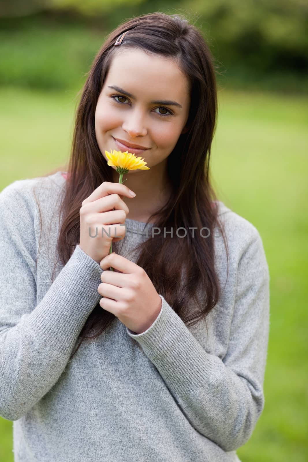 Young peaceful woman smelling a yellow flower while standing up in the countryside
