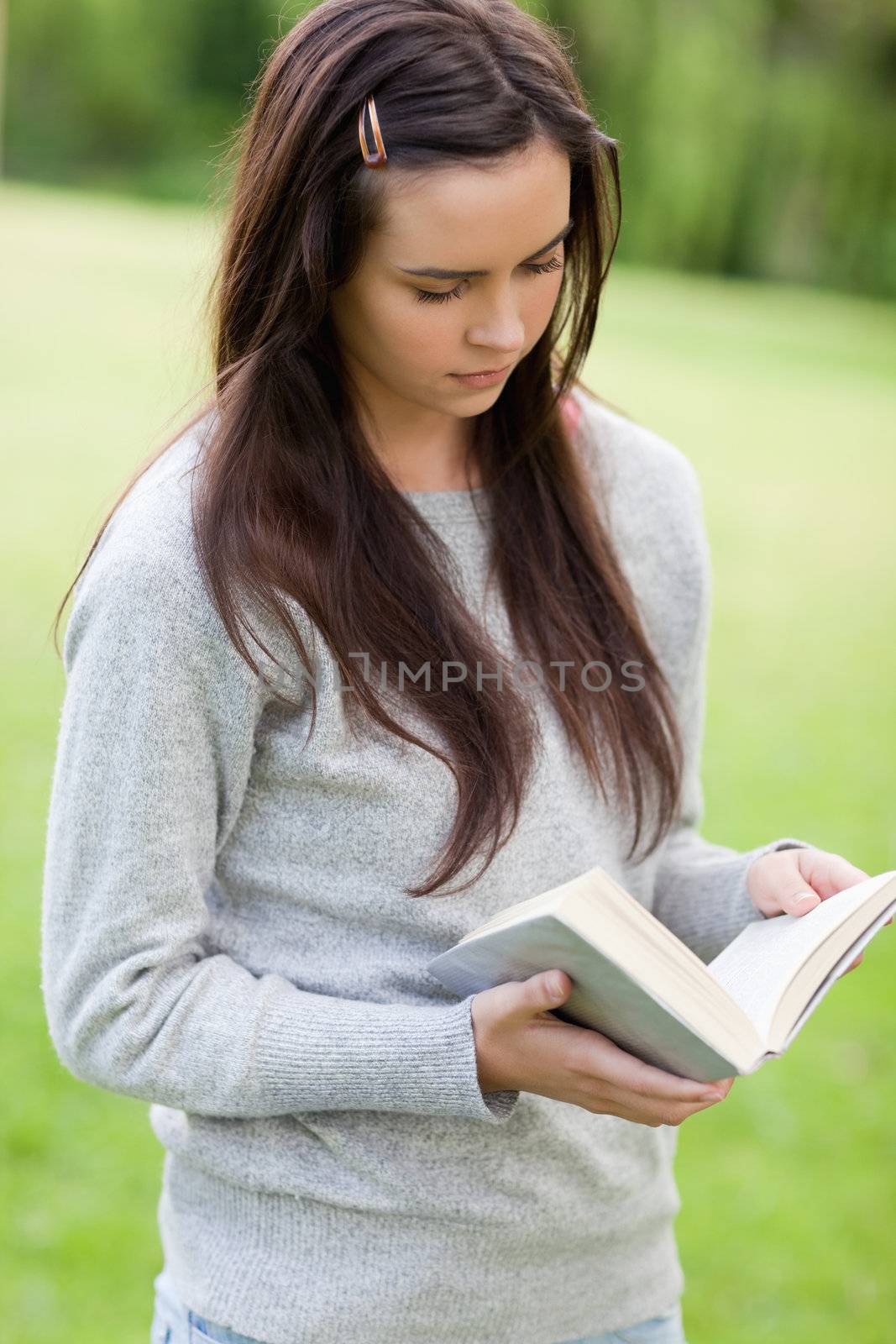 Serious young girl reading a book while standing upright in the countryside