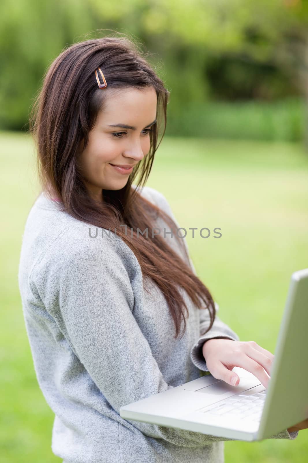 Happy young woman holding her laptop while standing upright in a parkland