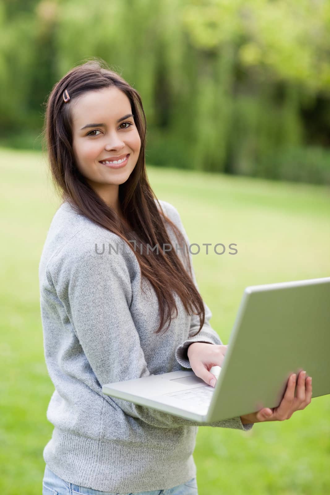 Young smiling woman holding her laptop while standing upright in by Wavebreakmedia